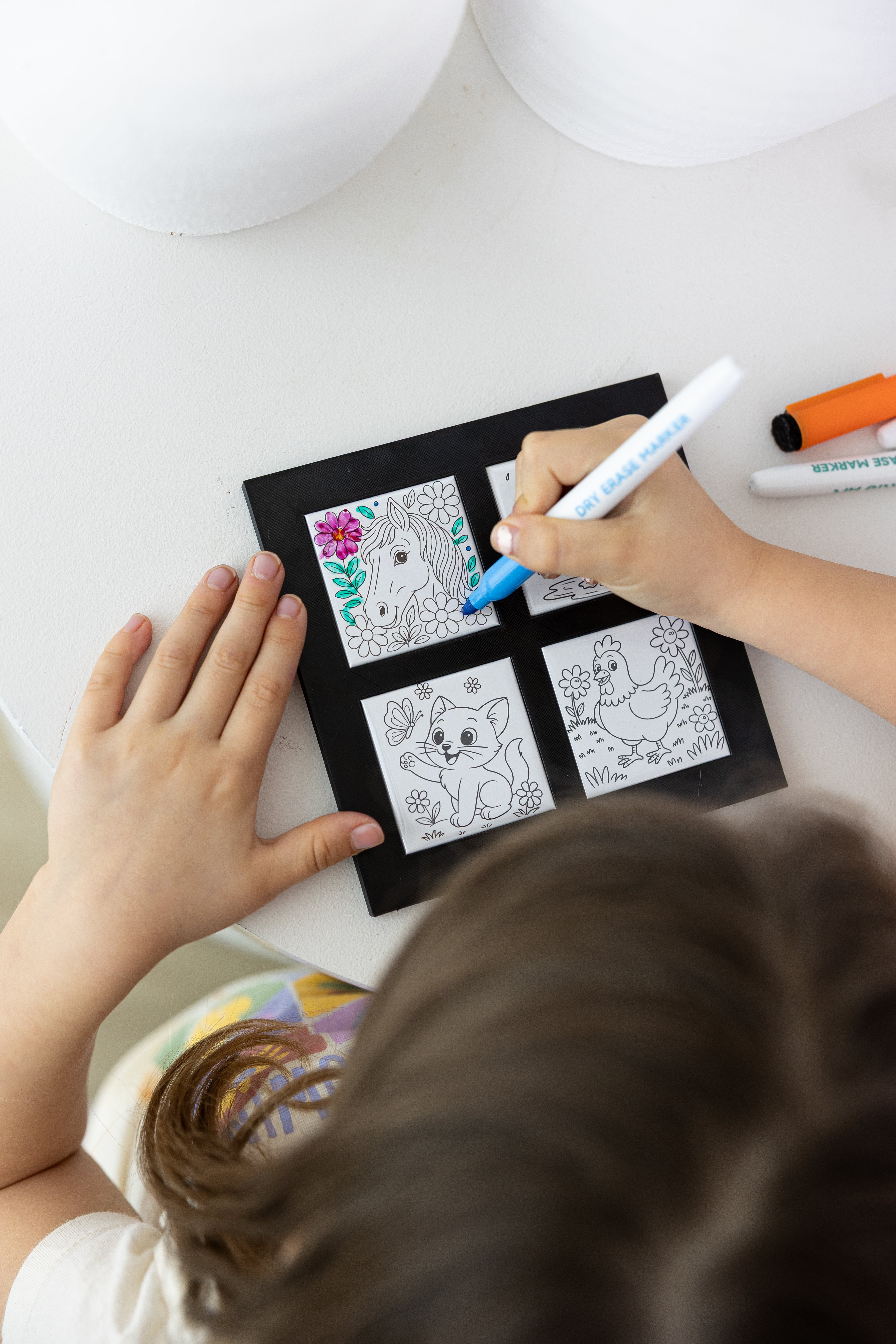 Child coloring a black frame with four animal illustrations on a white surface.